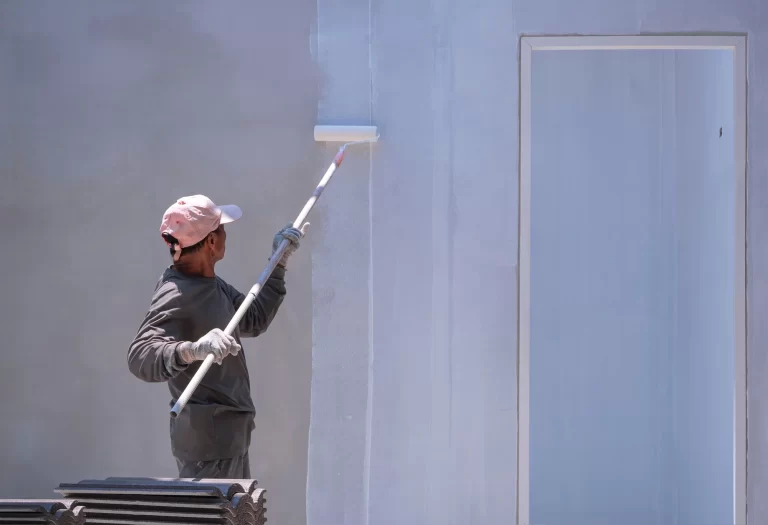 Construction worker painting primer white color on cement wall inside of house construction site